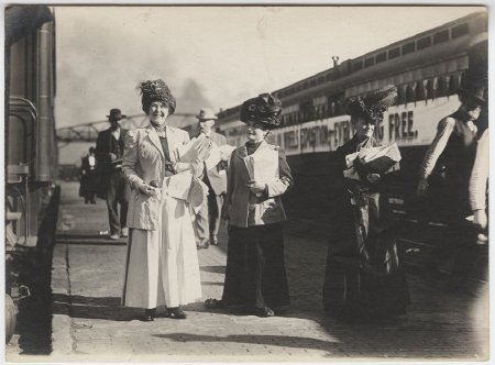 Three women standing beside a train.